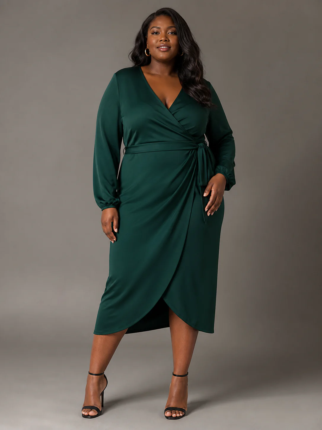 Plus-size Black model wearing an emerald green wrap midi dress in a warm-gray studio